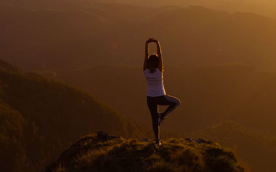 Mujer de espaldas practicando Yoga en lo alto de un pico de montaña